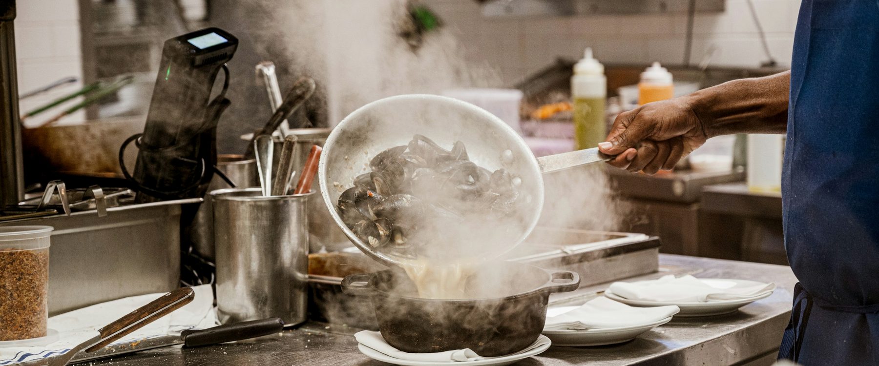Profissional preparando um prato em uma cozinha real de restaurante, em meio ao vapor da operação
